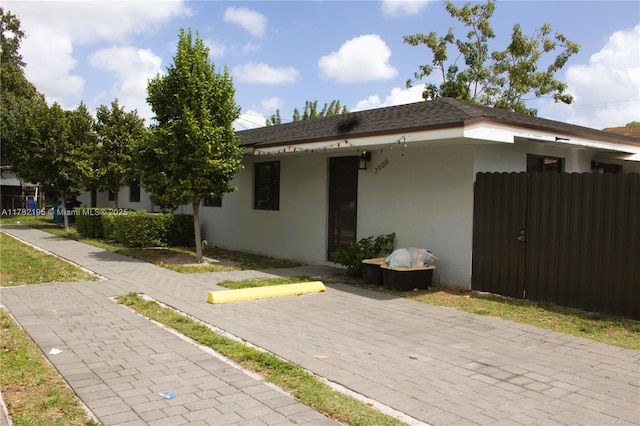 view of property exterior with stucco siding, uncovered parking, fence, and a shingled roof