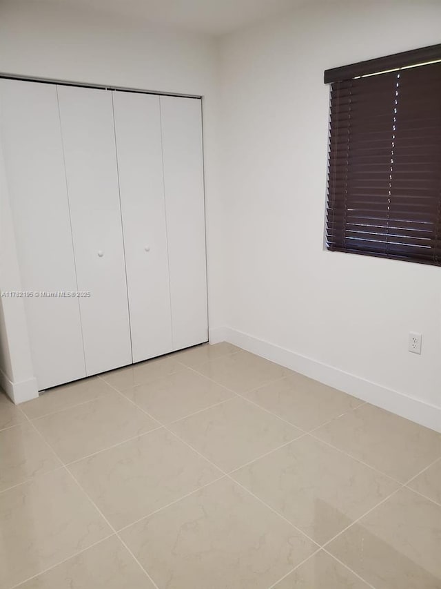 unfurnished bedroom with a closet, light tile patterned floors, and baseboards