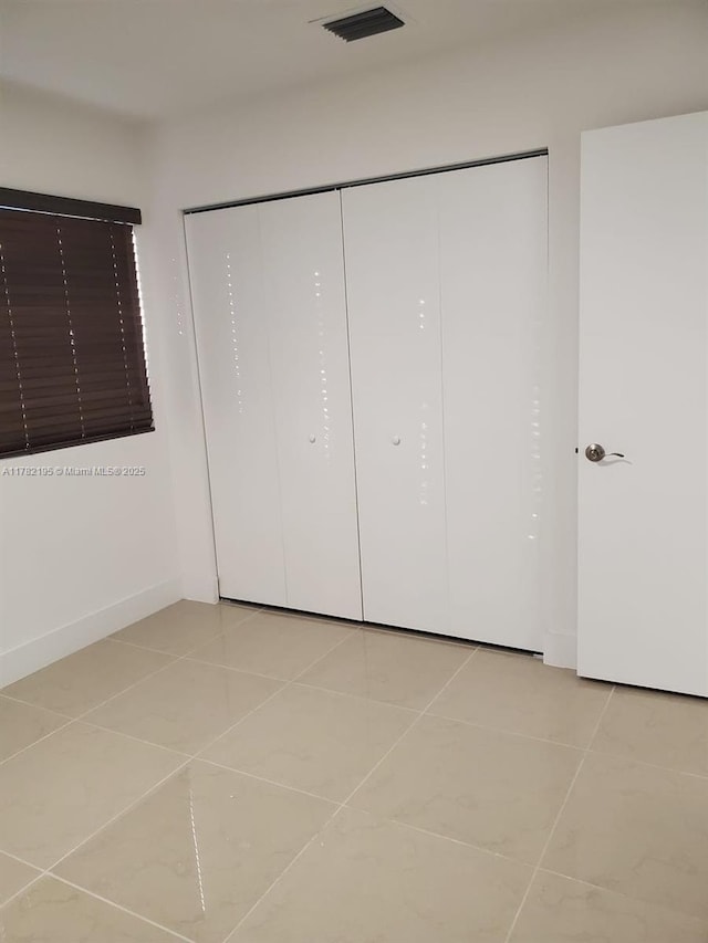 unfurnished bedroom featuring visible vents, baseboards, a closet, and light tile patterned flooring