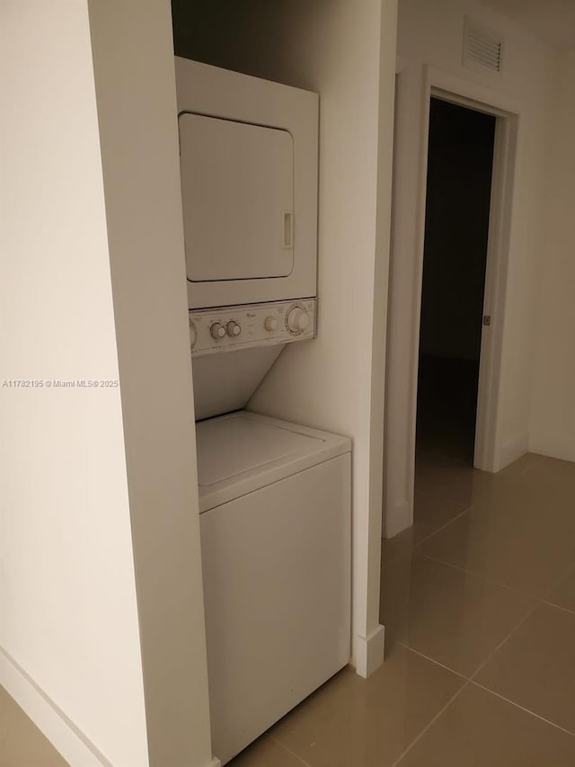laundry room featuring baseboards, tile patterned flooring, stacked washer / dryer, laundry area, and visible vents