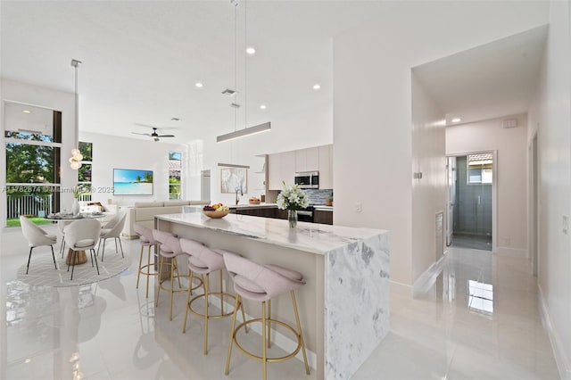 1807 Victoria Pointe Cir, Weston, FL 33327 - kitchen featuring stainless steel microwave, modern cabinets, a kitchen island, light stone counters, and a breakfast bar area