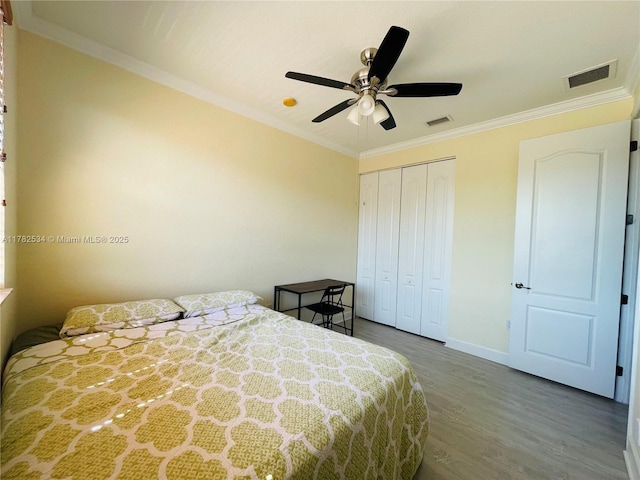 bedroom featuring a closet, baseboards, ornamental molding, visible vents, and wood finished floors