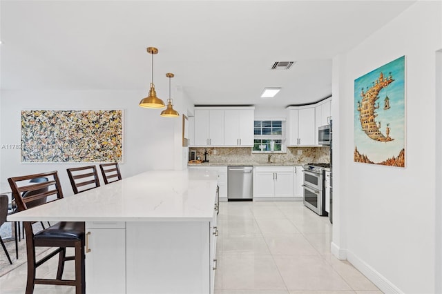 kitchen featuring tasteful backsplash, a kitchen breakfast bar, stainless steel appliances, white cabinets, and visible vents