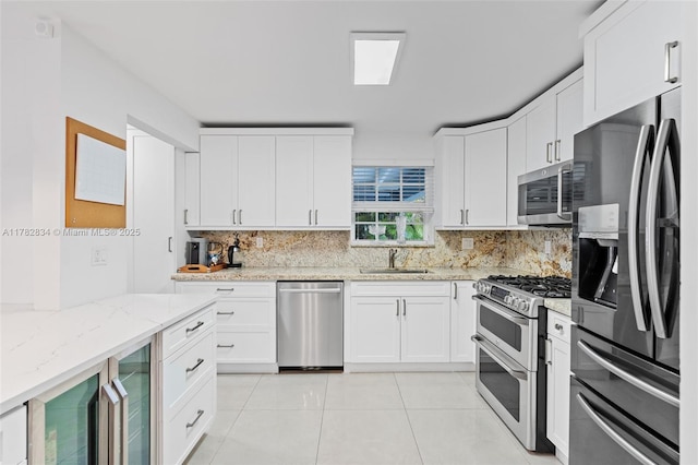 kitchen with a sink, white cabinets, light tile patterned floors, stainless steel appliances, and backsplash