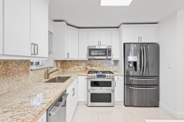 kitchen featuring white cabinets, stainless steel appliances, a sink, and light stone counters