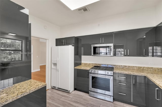 kitchen with visible vents, light wood-style floors, dark cabinets, light stone countertops, and stainless steel appliances