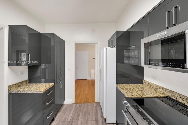 kitchen with baseboards, modern cabinets, appliances with stainless steel finishes, light wood finished floors, and light stone countertops