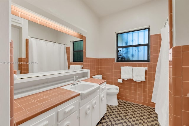 full bath featuring vanity, a wainscoted wall, toilet, tile walls, and tile patterned floors
