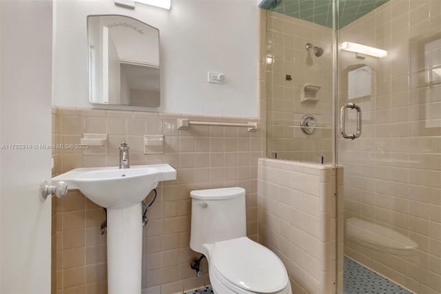 bathroom with toilet, wainscoting, tile walls, and a stall shower