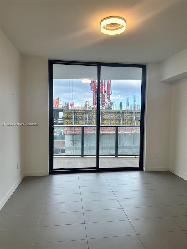 unfurnished room featuring floor to ceiling windows, tile patterned floors, a view of city, and baseboards