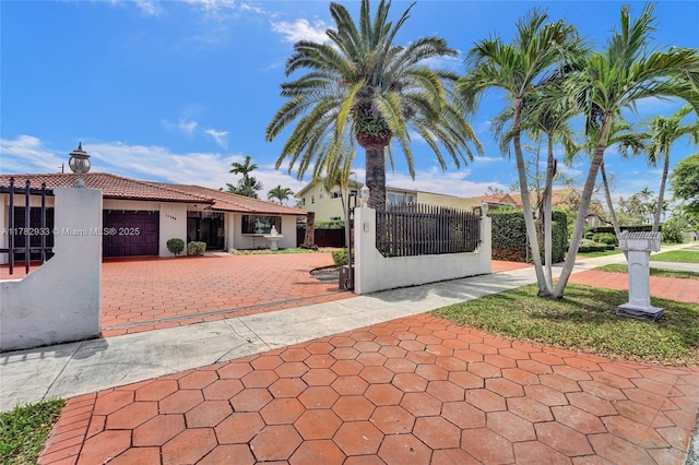 view of front of house with stucco siding, driveway, a fenced front yard, a garage, and a tiled roof