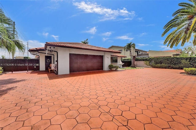 mediterranean / spanish home with a tiled roof, a garage, fence, stucco siding, and decorative driveway