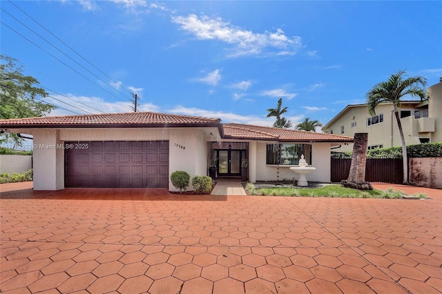 view of front facade with an attached garage, a tile roof, fence, stucco siding, and decorative driveway