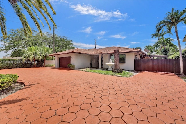 ranch-style home featuring a garage, fence, stucco siding, a gate, and decorative driveway