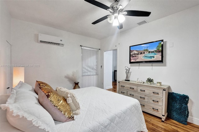 bedroom featuring an AC wall unit, baseboards, light wood-style floors, visible vents, and ceiling fan