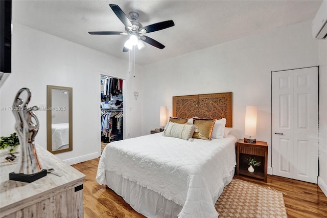 bedroom featuring light wood finished floors, baseboards, a wall unit AC, and ceiling fan