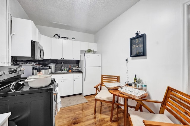 kitchen featuring tasteful backsplash, electric range oven, a sink, freestanding refrigerator, and light wood-style floors