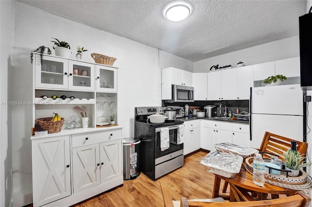 kitchen featuring glass insert cabinets, a textured ceiling, white cabinets, stainless steel appliances, and light wood finished floors