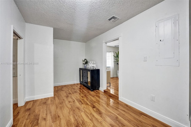 spare room featuring baseboards, light wood-type flooring, electric panel, a textured ceiling, and visible vents