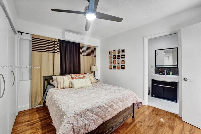 bedroom featuring baseboards, a sink, ceiling fan, wood finished floors, and a wall unit AC
