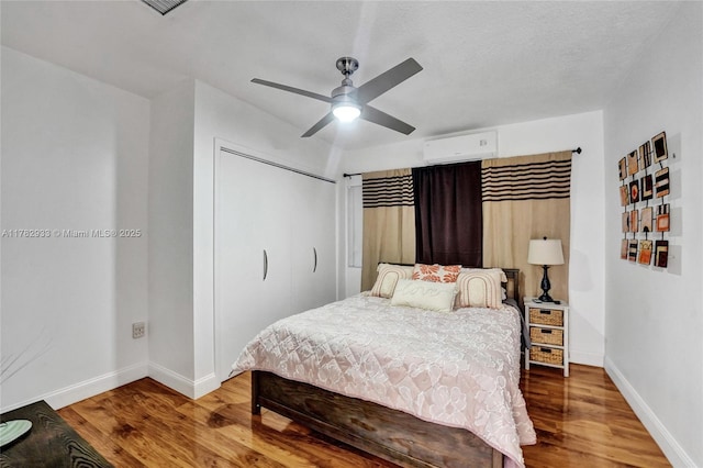 bedroom featuring a closet, baseboards, a wall mounted AC, and wood finished floors