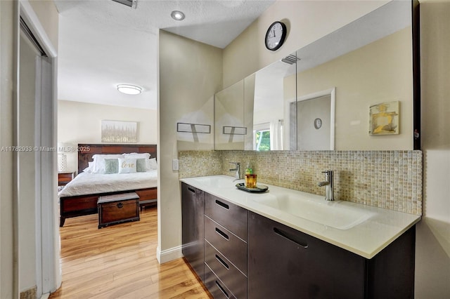 ensuite bathroom with tasteful backsplash, a sink, connected bathroom, and wood finished floors
