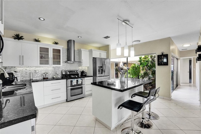 kitchen with wall chimney range hood, visible vents, a breakfast bar, a sink, and stainless steel appliances