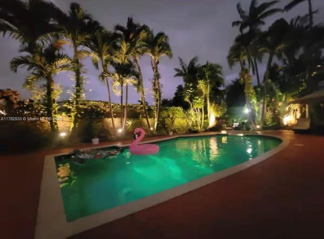 pool at night with a patio and an outdoor pool