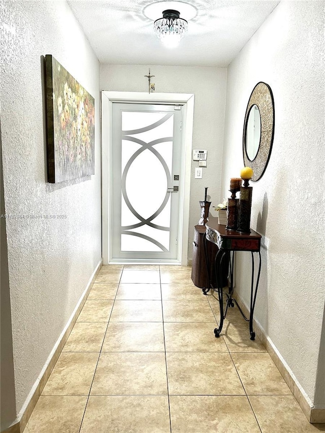 doorway featuring a textured ceiling, a textured wall, baseboards, and light tile patterned floors
