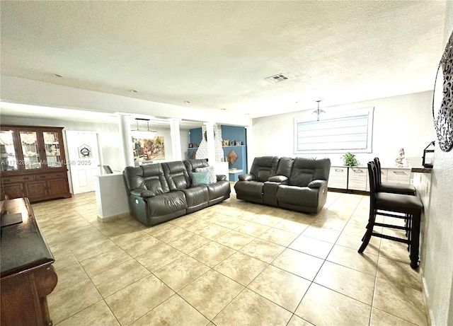 living area with decorative columns, light tile patterned floors, visible vents, and a textured ceiling