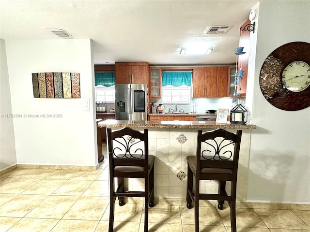 kitchen with a peninsula, stainless steel fridge with ice dispenser, a sink, and visible vents