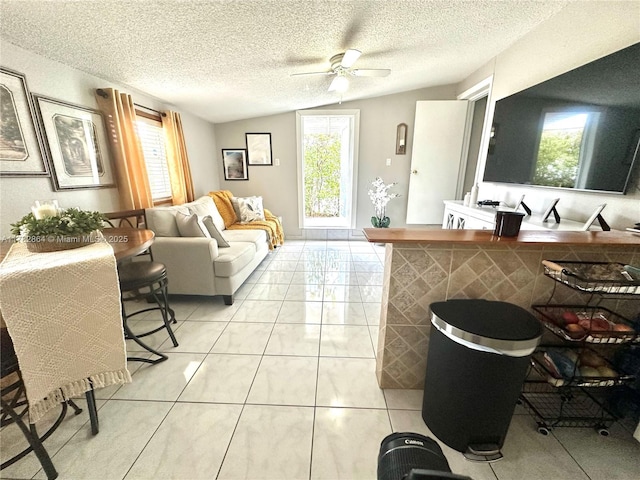 living area with light tile patterned floors, a ceiling fan, lofted ceiling, and a textured ceiling