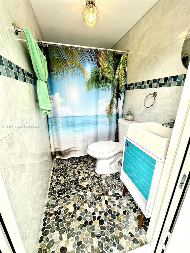 full bath with stone finish flooring, toilet, curtained shower, a sink, and tile walls