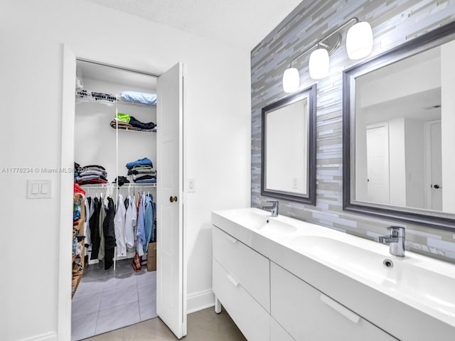 bathroom featuring baseboards, double vanity, tile patterned flooring, a walk in closet, and a sink