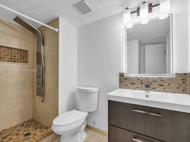 bathroom with visible vents, toilet, vanity, tiled shower, and tile patterned flooring