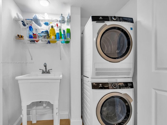 clothes washing area with stacked washer / dryer, laundry area, and baseboards