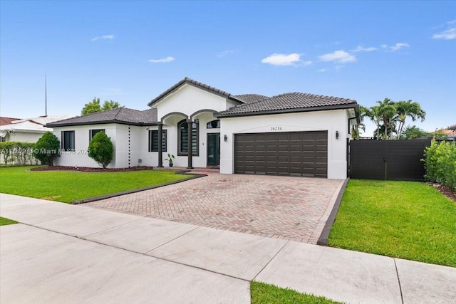 view of front of house with a tiled roof, stucco siding, decorative driveway, a front yard, and an attached garage