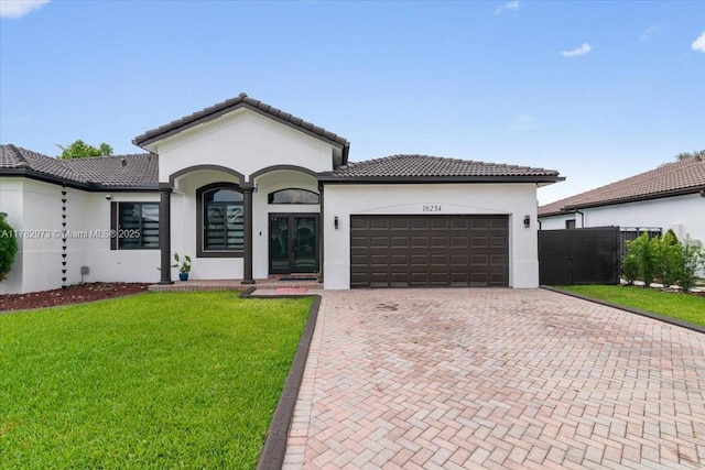 single story home with a garage, a tile roof, stucco siding, a front lawn, and decorative driveway