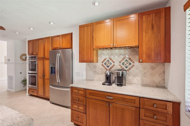 kitchen with stainless steel appliances, brown cabinets, backsplash, and light stone counters