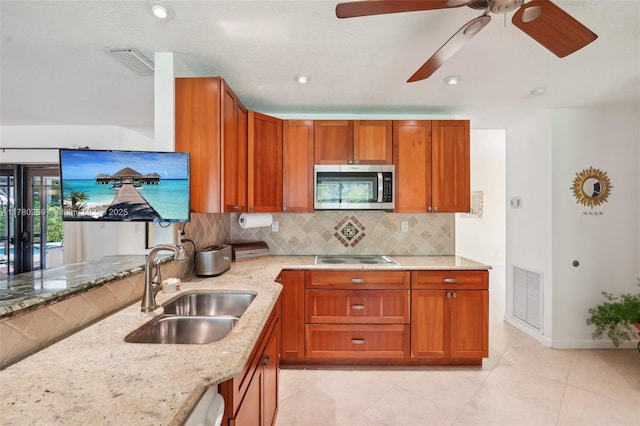 kitchen with stainless steel microwave, light stone countertops, visible vents, and a sink