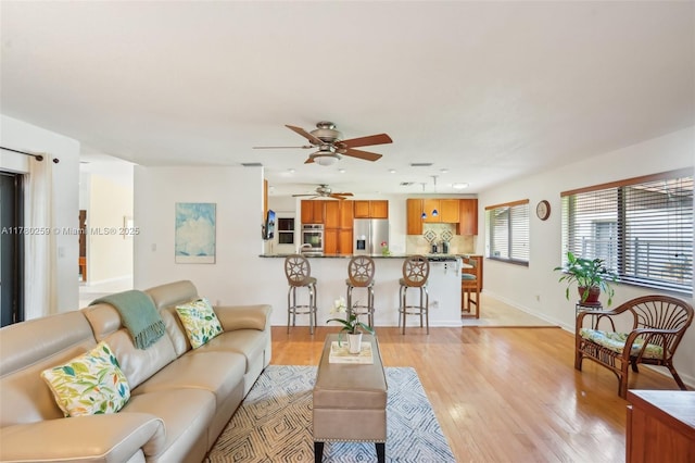 living area featuring baseboards, a ceiling fan, and light wood finished floors