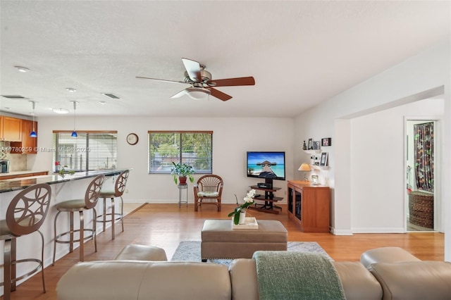 living area with visible vents, light wood-type flooring, baseboards, and ceiling fan