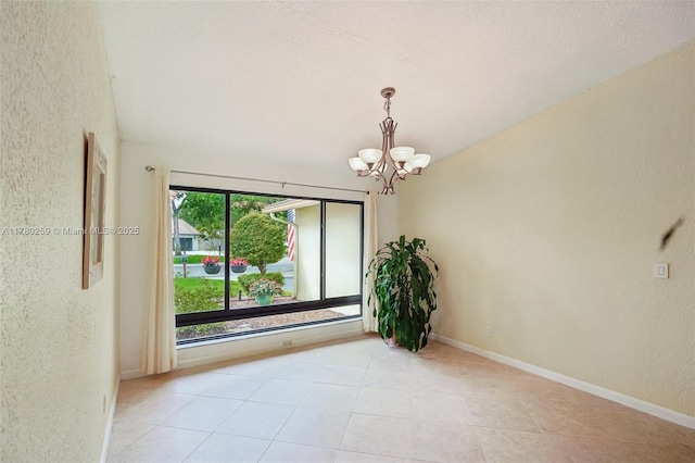 tiled spare room with baseboards, an inviting chandelier, and a textured wall