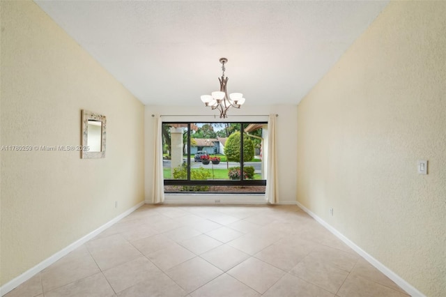 spare room with a chandelier, a textured wall, baseboards, and light tile patterned flooring