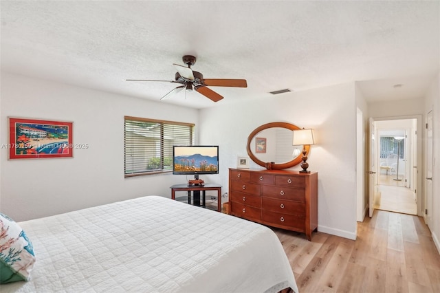 bedroom featuring baseboards, light wood-type flooring, a textured ceiling, a ceiling fan, and visible vents