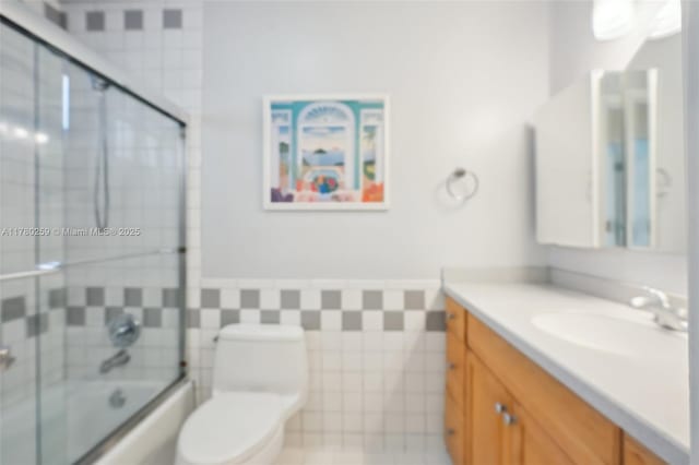 full bath featuring shower / bath combination with glass door, vanity, toilet, wainscoting, and tile walls