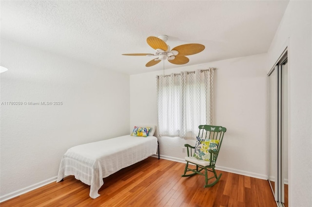 bedroom featuring a closet, baseboards, a textured ceiling, ceiling fan, and wood finished floors