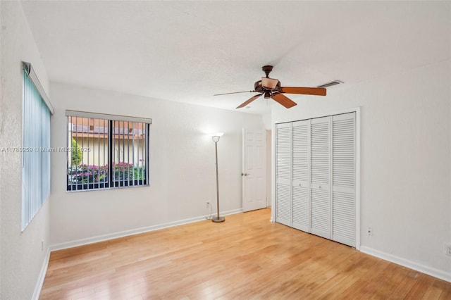 unfurnished bedroom with a closet, a ceiling fan, visible vents, hardwood / wood-style floors, and baseboards