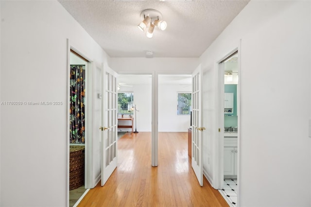 hall with light wood-style floors, french doors, a textured ceiling, and baseboards