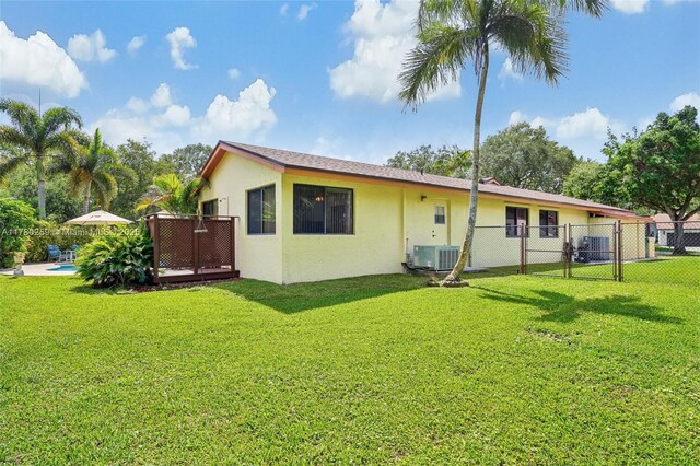 back of house with a yard, fence, central AC unit, and stucco siding